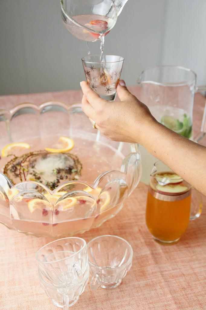 a woman's hand pouring punch into a small glass with a punchbowl in the background